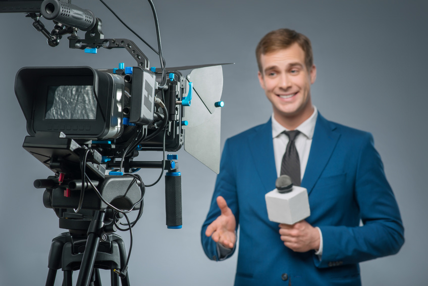 Smiling reporter. Handsome smiling newscaster upholding his microphone and leading the news.